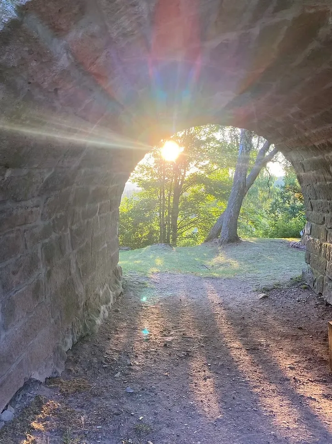 Seelenfarbe – Achtsamkeitstrainerin und Gesundheitspraktikerin (DGAM) – malerischer Blick durch einen steinernen Torbogen, möglicherweise einen Tunnel oder eine Unterführung, mit Blick auf eine helle, sonnenbeschienene Naturlandschaft